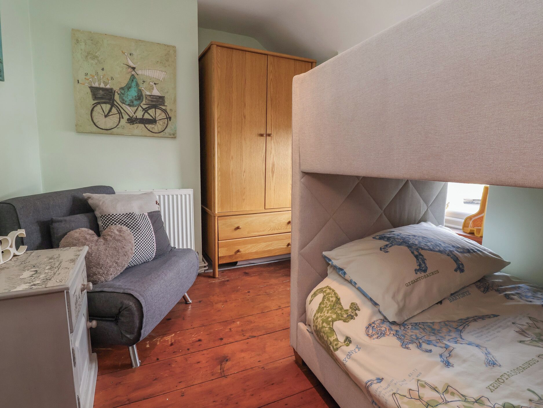 Een slaapkamer met een stapelbed, een slaapbank, een houten kledingkast en een fietsprint op de muur.