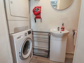 Une petite buanderie équipée d’un lave-linge Bosch, d’un évier et d’un étendoir.