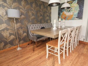 Een eetruimte met een houten tafel, witte stoelen, een knooptapijtbank en een vloerlamp.