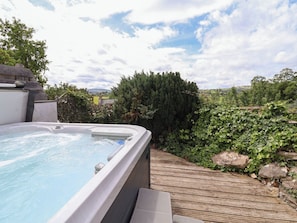 Un bain à remous avec une terrasse en bois, entouré de verdure et offrant une vue sur la campagne.