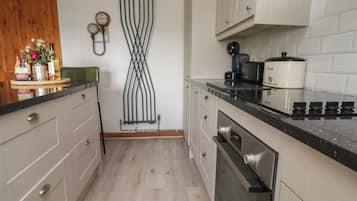 A kitchen with white cabinets, a black countertop, a built-in oven, and a coffee maker.