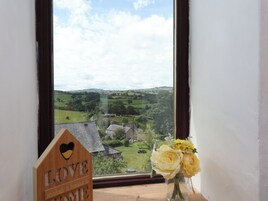 Vista a través de una ventana con un letrero de madera que dice 'LOVE makes a home' y un jarrón con flores amarillas.