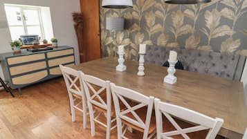A dining area with a wooden table, white chairs, two pendant lights, and a grey upholstered bench.