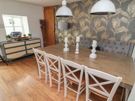 Un comedor con una mesa de madera, sillas blancas, dos lámparas colgantes y un banco tapizado gris.