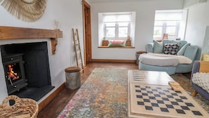 A cozy living room with a fireplace, a checkered coffee table, a colorful rug, and a blue sofa.