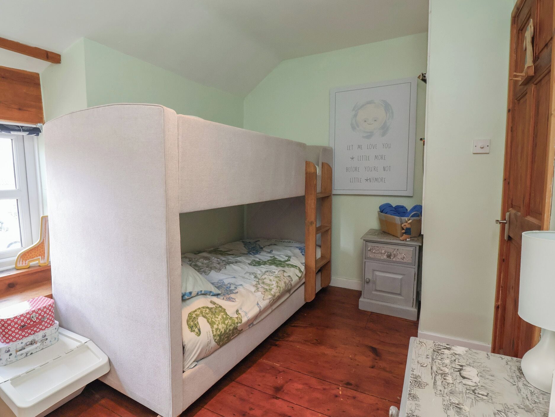 A bunk bed with a floral bedspread, a small dresser with a toy on top, and a framed quote on the wall.