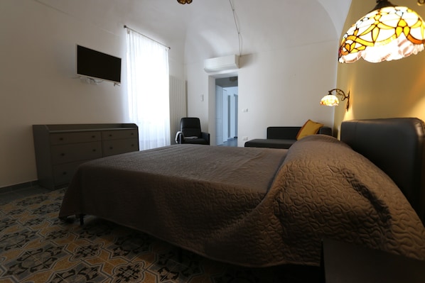 Una camera da letto con un letto, una cassettiera, una sedia, un televisore e una lampada.