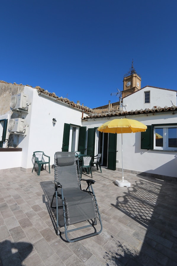 A patio with a table and chairs, a yellow umbrella, and a clock tower in the background.