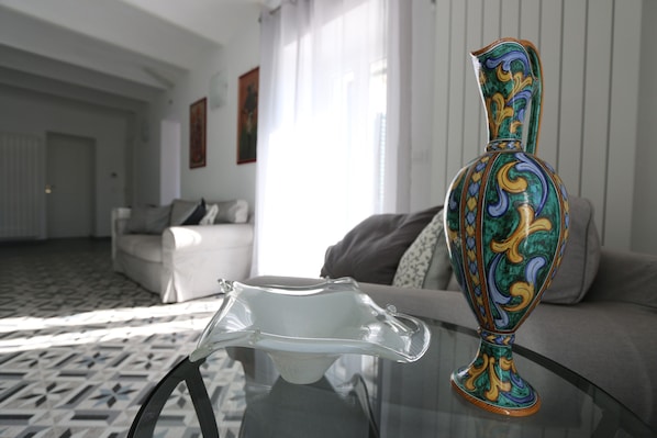 A room with a glass table, a decorative vase, a sofa, and a patterned carpet.