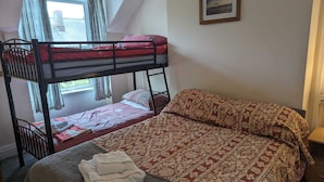 Ein Zimmer mit einem Etagenbett, einem Einzelbett, einer gemusterten Tagesdecke, einem gerahmten Bild an der Wand und einem Fenster mit Vorhängen.
