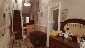 Ein Flur mit Treppe, einem roten Sessel, einer Holzkommode und einem gefliesten Boden.