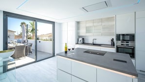 Una cucina moderna con una grande isola, forno integrato e una porta vetrata che dà su un balcone con mobili da esterno.