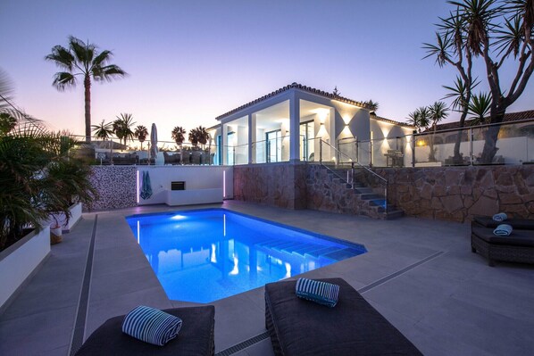 A swimming pool with a glass-enclosed lounge area, stone walls, and palm trees. - Villa Las Farolas - El Faro Luxury Villa (Mijas Costa)