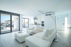A modern living room with a white sofa, a coffee table, and a large window. - Villa Las Farolas - El Faro Luxury Villa (Mijas Costa)