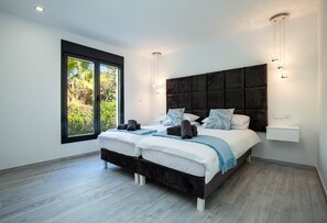 A modern bedroom with two beds, a large window, and a view of greenery. - Villa Las Farolas - El Faro Luxury Villa (Mijas Costa)