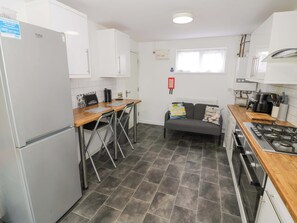 Eine kompakte Küche mit Kühlschrank, Herd und einer kleinen Essecke mit Stühlen und einer Couch.