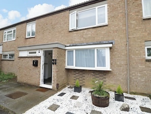 A two-story brick house with a front door, a small garden with potted plants, and a gravel pathway. - Lodge Park (Corby)