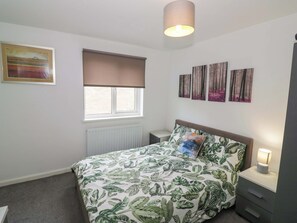 Een slaapkamer met een bed, een raam met zonwering, een radiator, een nachtkastje met een lamp en decoratie aan de muur.