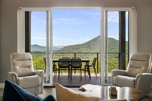 Ein Zimmer mit einer Glasschiebetür, die auf eine Außenterrasse mit Tisch und Stühlen, zwei Sesseln und einem Holztisch führt.