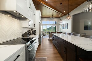 A modern kitchen with a large island, built-in appliances, and a view to the outdoors. - Elevated Escapes by Carolina Mornings | Luxury w/PERFECT mountain views near AVL (Candler)