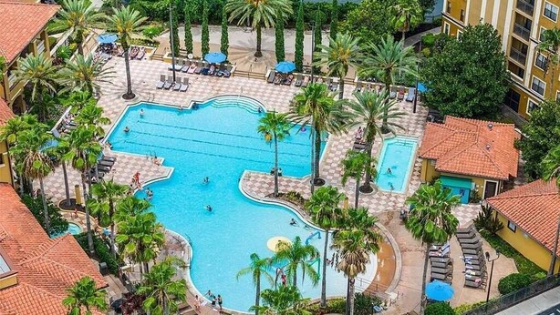 Ein großer Pool im Freien, umgeben von Palmen und Liegestühlen, mit Blick auf eine Stadtkulisse im Hintergrund.