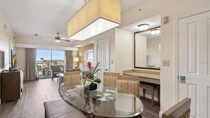 Ein Hotelzimmer mit einem Glastisch, Korbstühlen, einer Couch, einem Deckenventilator und einem großen Fenster mit Blick.