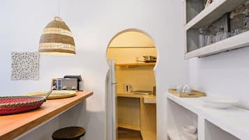 Une cuisine étroite avec un plan de travail en bois, des tabourets, un luminaire suspendu et une porte-fenêtre donnant sur un coin repas.