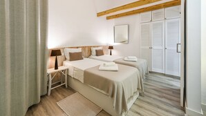 A bedroom with two beds, wooden beams, a mirror, and a wardrobe with louvered doors. - Casa Amarela (Mértola)