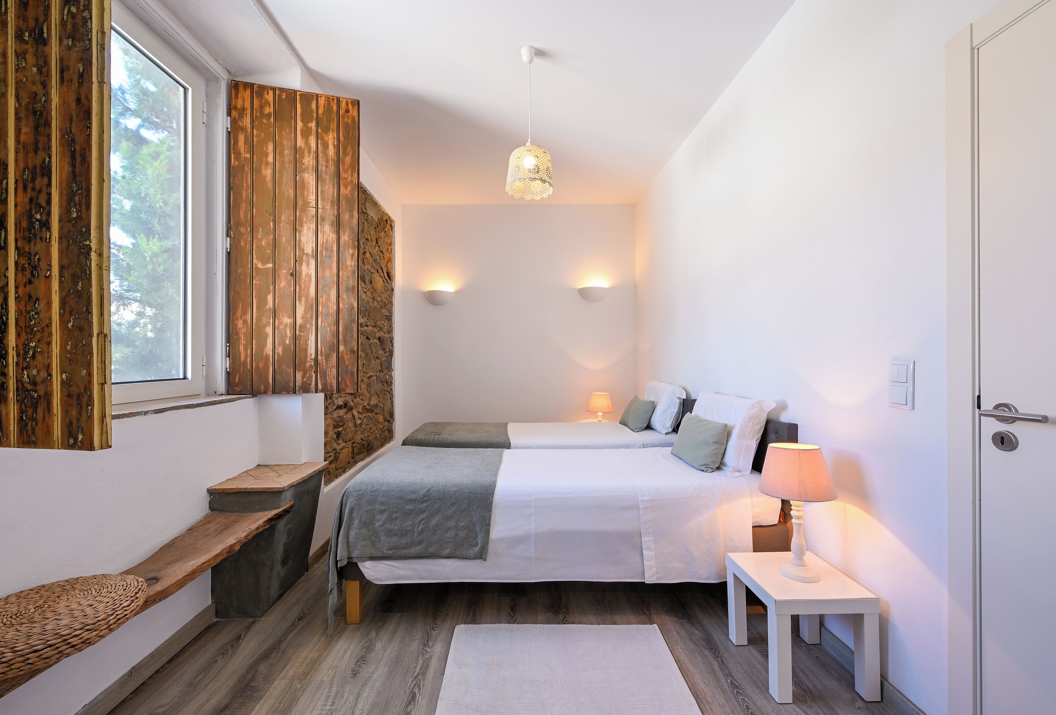 Ein Schlafzimmer mit einem großen Bett, Nachttischen, einer Bank, einer Steinwand und einer Pendelleuchte.