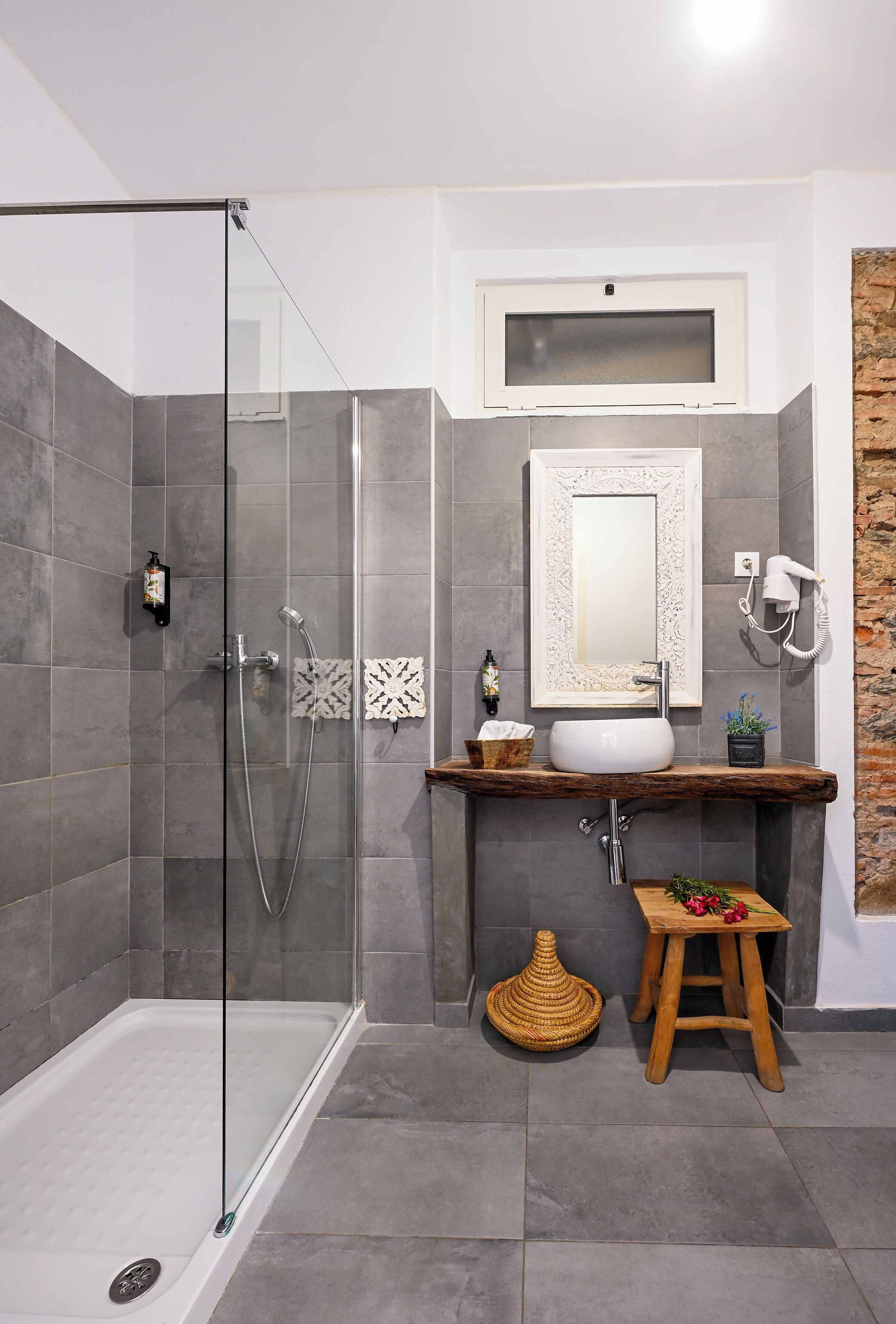 Un baño moderno con cabina de ducha de vidrio, tocador con lavamanos, secador de pelo y un espejo decorativo.
