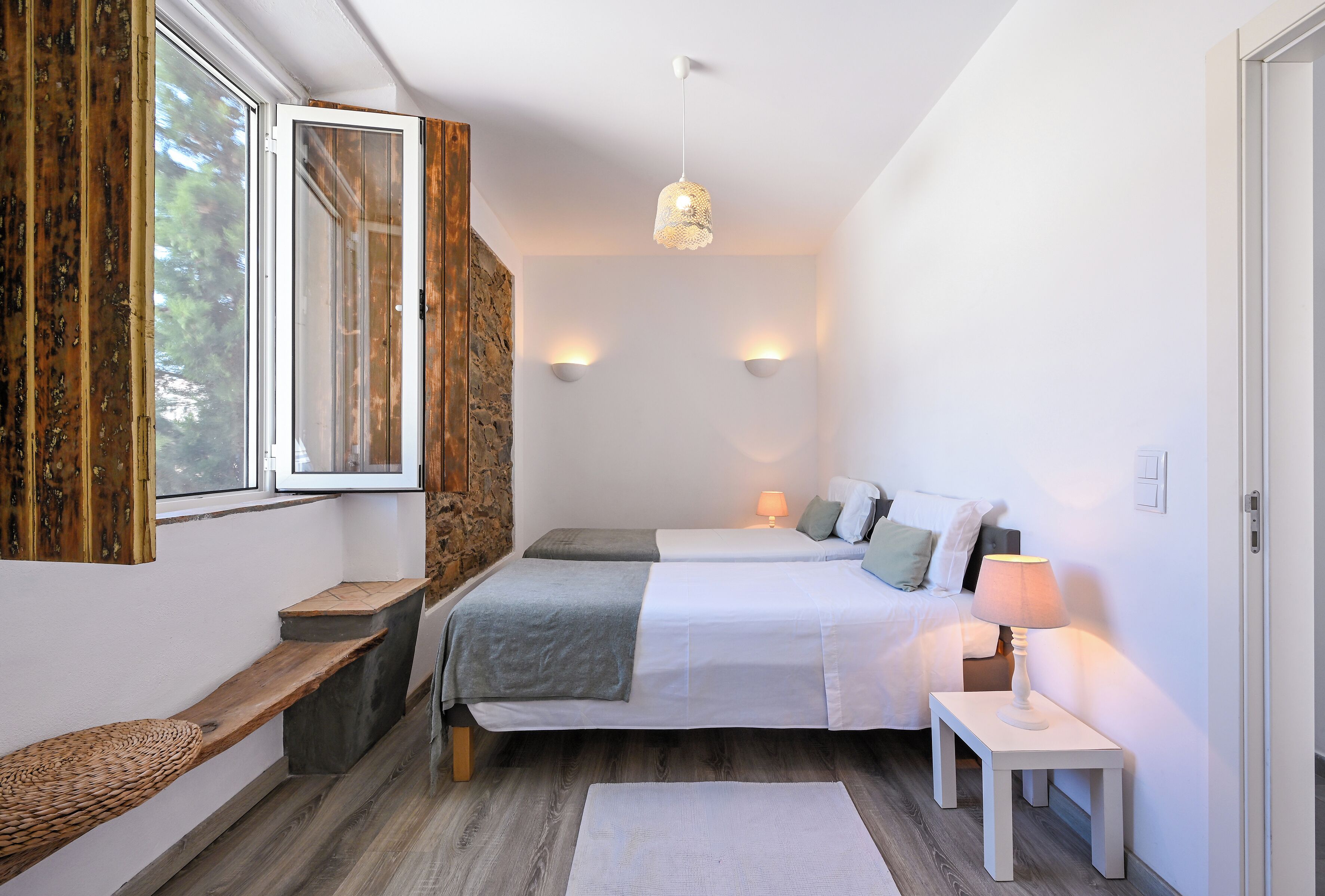 A bedroom with a bed, bedside tables, a bench, a window, and a wall-mounted light fixture.