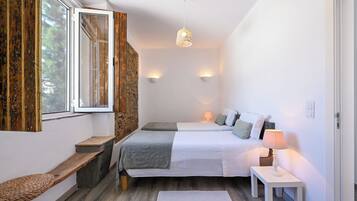A bedroom with a bed, bedside tables, a bench, a window, and a wall-mounted light fixture.