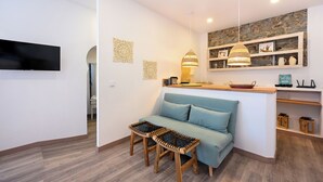 A modern living room with a sofa, two wooden stools, a flat-screen TV, decorative wall art, a hanging pendant light, and a stone wall accent. - Casa Amarela (Mértola)