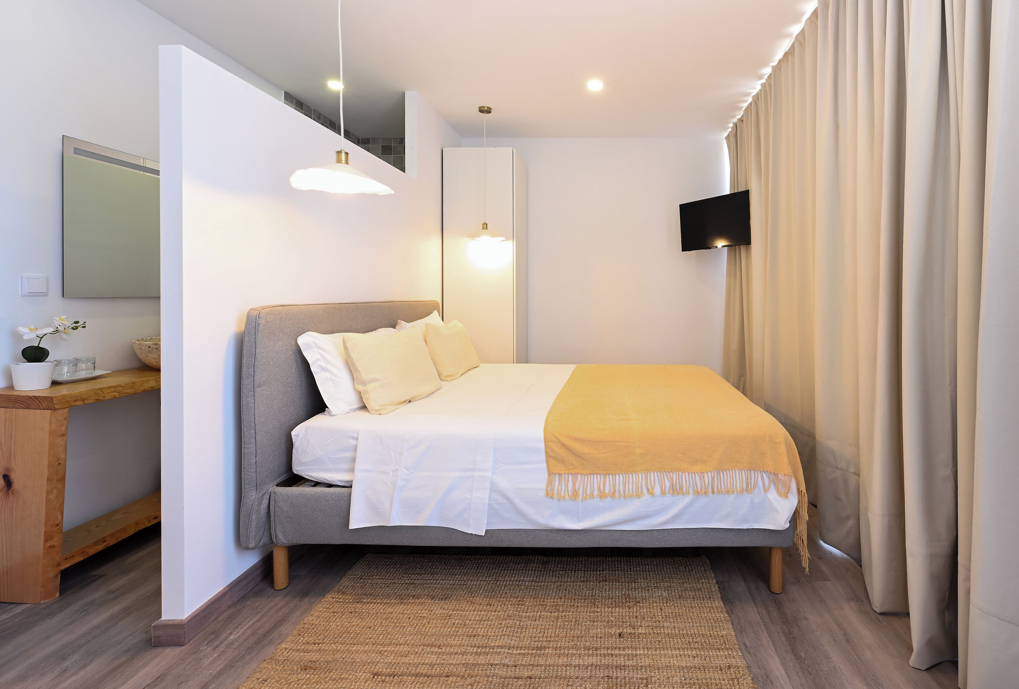 A modern bedroom with a bed, bedside table, mirror, and a TV mounted on the wall.