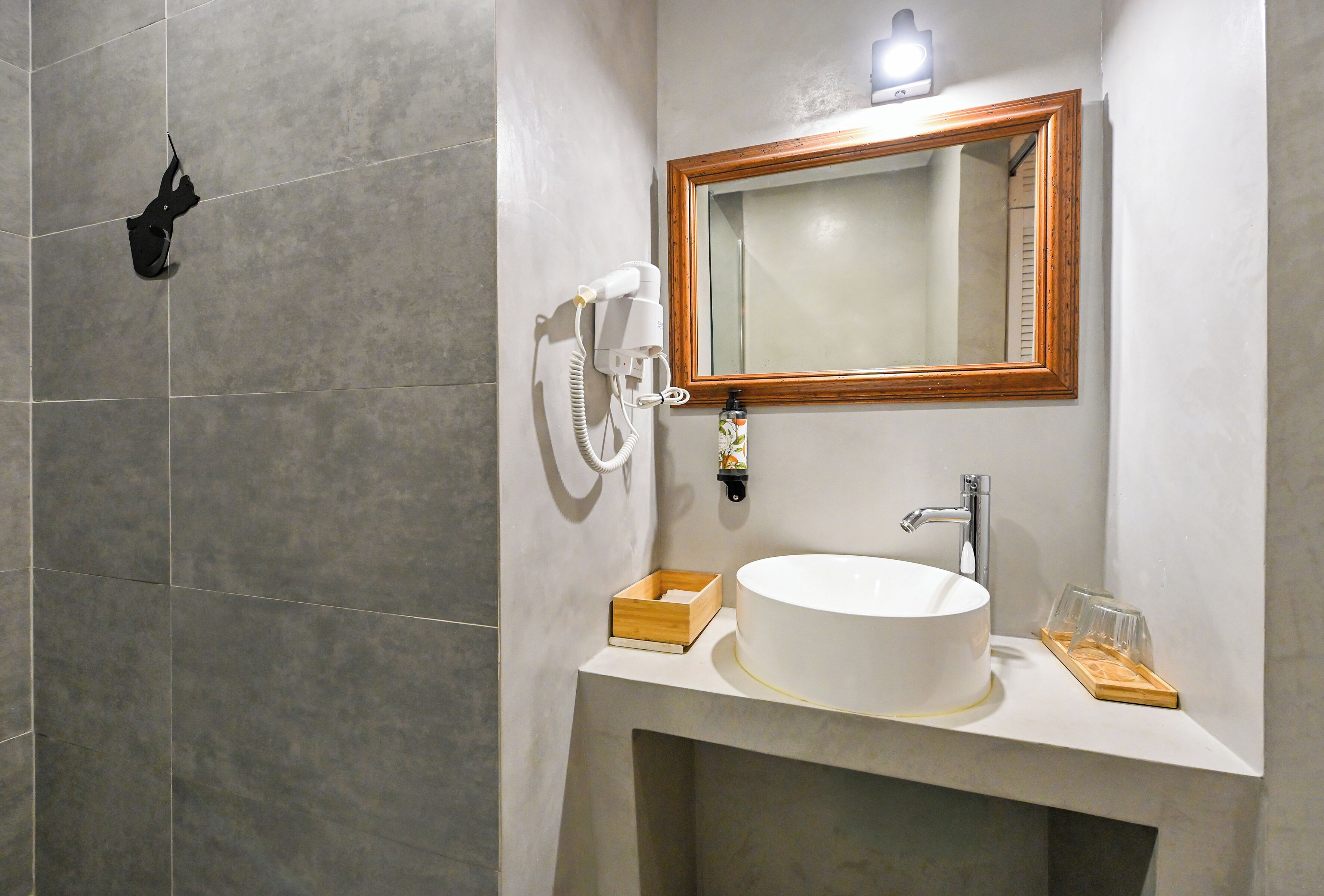 Un baño con un lavamanos blanco, un espejo con marco de madera y un cabezal de ducha manual.