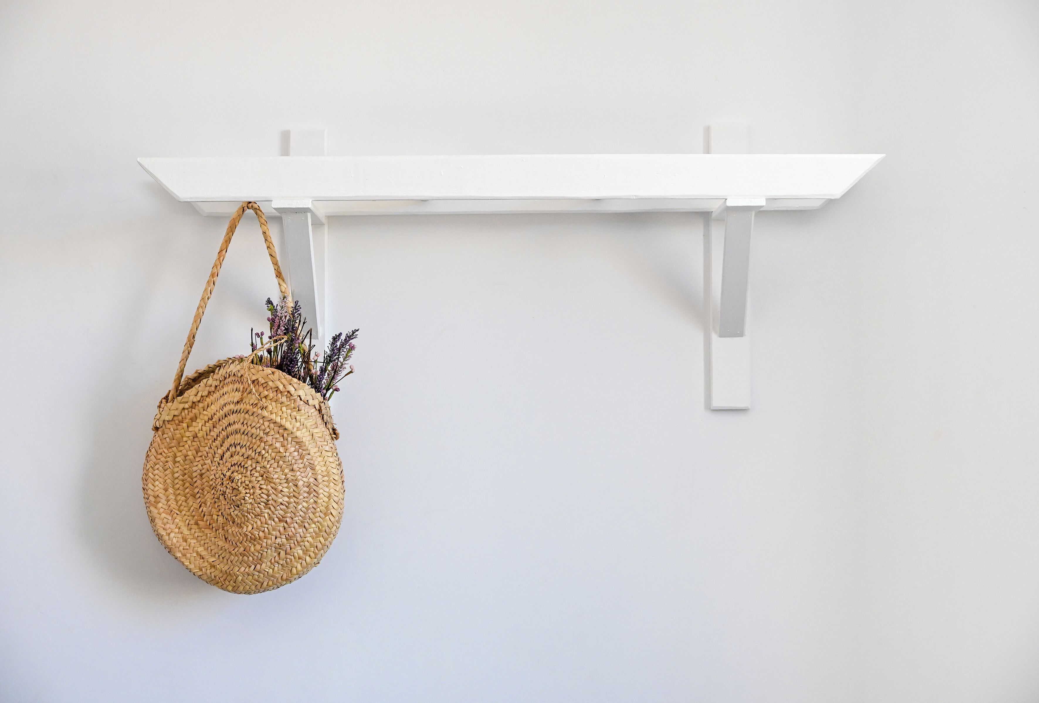 A round woven bag hanging on a white wall-mounted shelf.
