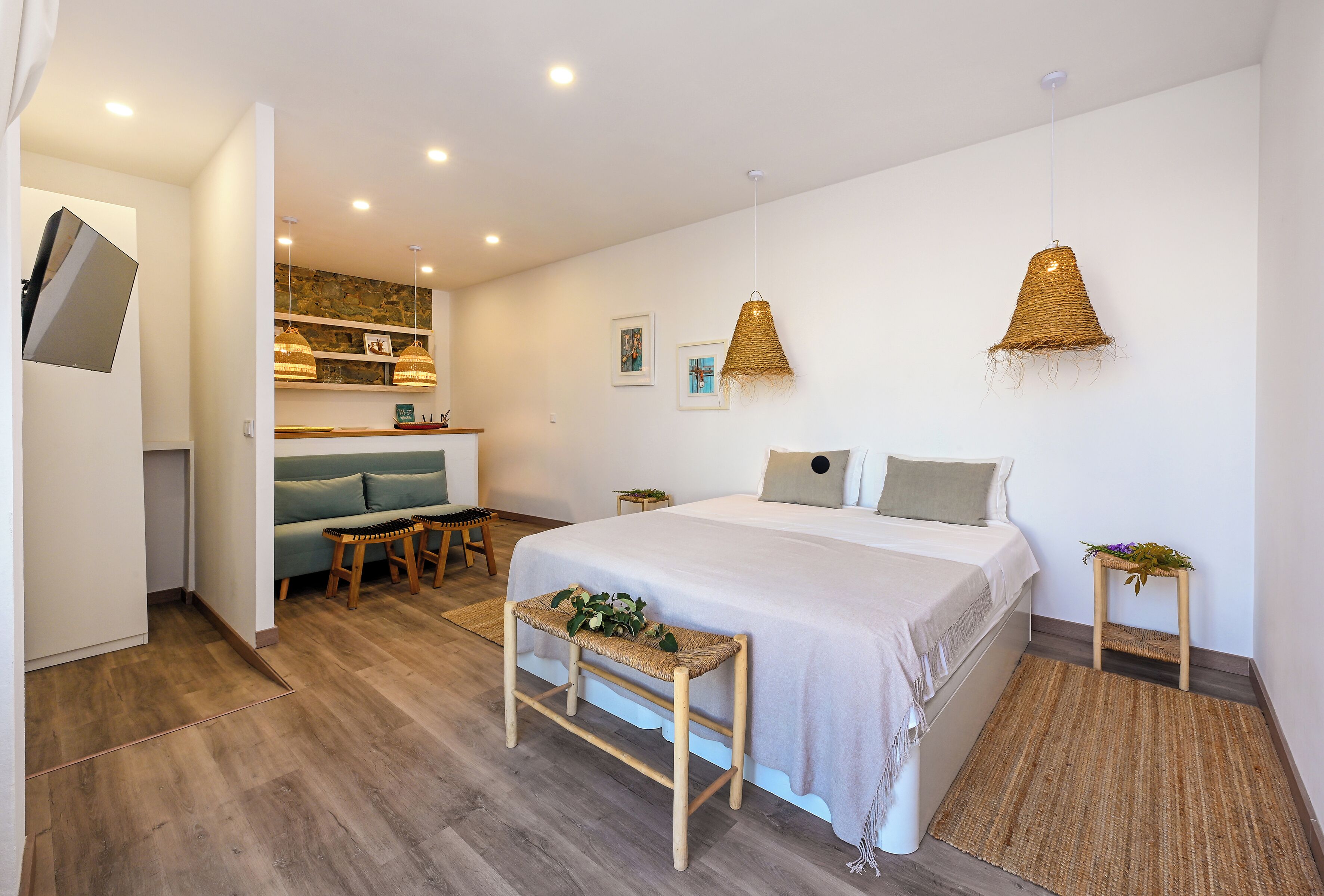 A modern bedroom with a bed, bedside tables, a sofa, and a small kitchen area.