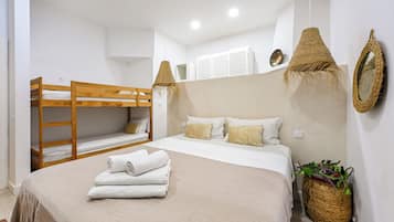 Un dormitorio con una cama doble, una cama individual con almohadas, una toalla enrollada, una cesta tejida con plantas y un espejo montado en la pared.
