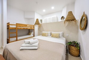 A bedroom with a bunk bed, a single bed with pillows, a rolled towel, a woven basket with plants, and a wall-mounted mirror.
