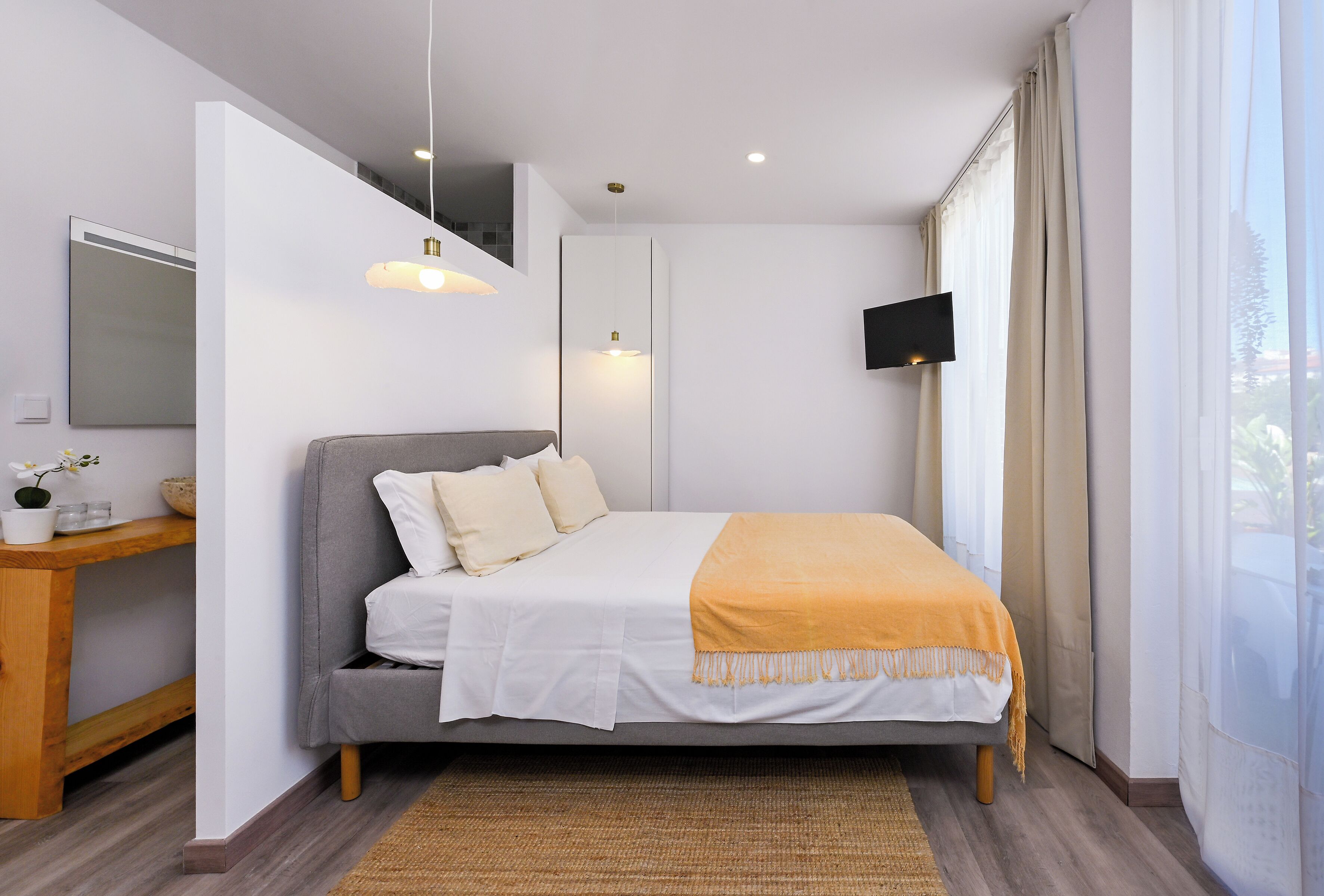 A modern bedroom with a bed, bedside table, and a TV mounted on the wall.