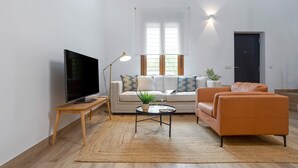 Una sala de estar con sofá, mesa de centro, televisión y lámpara.