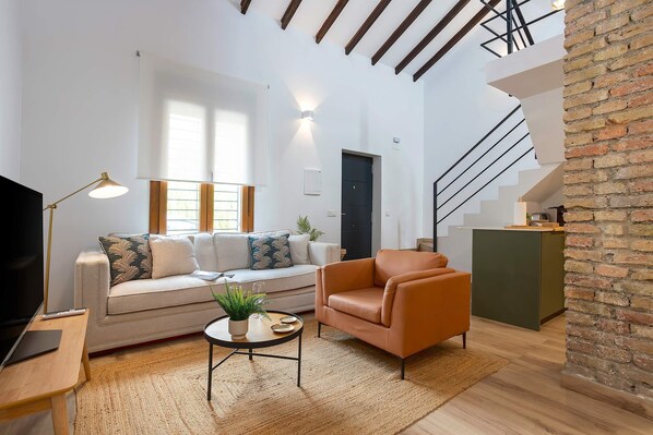 Ein modernes Wohnzimmer mit Sofa, Sessel, Couchtisch und Fernseher.