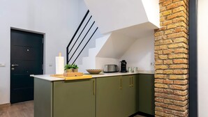 Una cocina con una puerta oscura, armarios verdes, una encimera blanca, un tostador, un tazón y una pared de ladrillo.