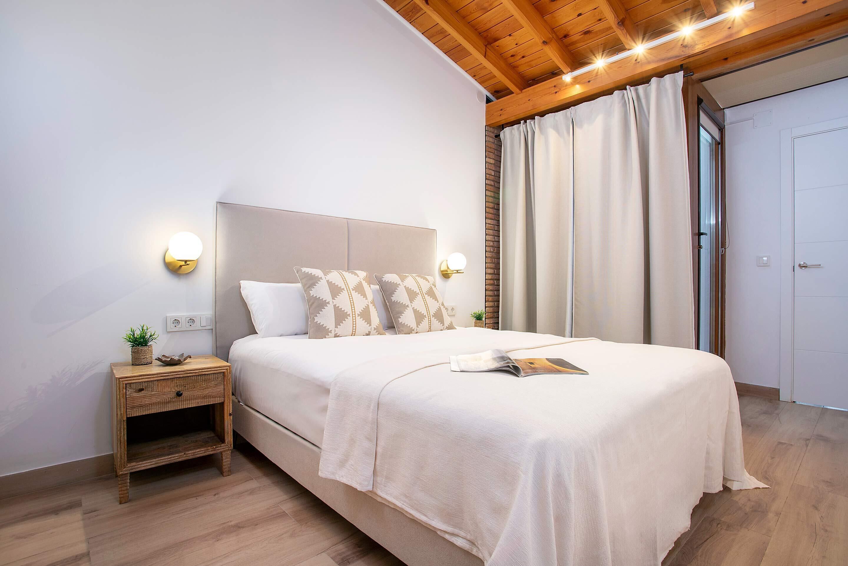 Un dormitorio con cama, mesita de noche, luces fijadas a la pared y una puerta.