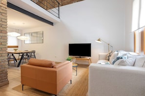 Ein modernes Wohnzimmer mit Sofa, Fernseher und Essbereich mit Tisch und Stühlen.