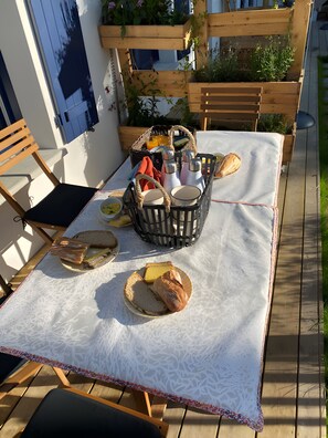 Ein Essbereich im Freien mit einem Tisch für zwei Personen, ausgestattet mit einer weißen Tischdecke, Holzstühlen und einem Korb voller Speisen.