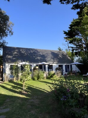 Ein Haus mit geneigtem Dach, einem umzäunten Garten und einer Bepflanzung mit verschiedenen Blumen und Pflanzen.