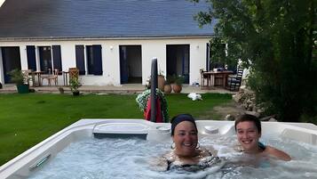 Un jacuzzi con dos personas, rodeado por un césped y un edificio con techo inclinado.