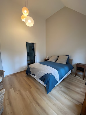 Une chambre à coucher comprenant un lit, des tables de chevet, un luminaire suspendu et une porte donnant sur une autre pièce.