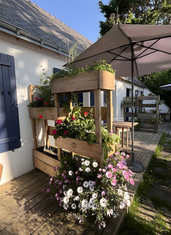 Un bac à fleurs en bois, orné de fleurs, et une table placée sous une pergola.